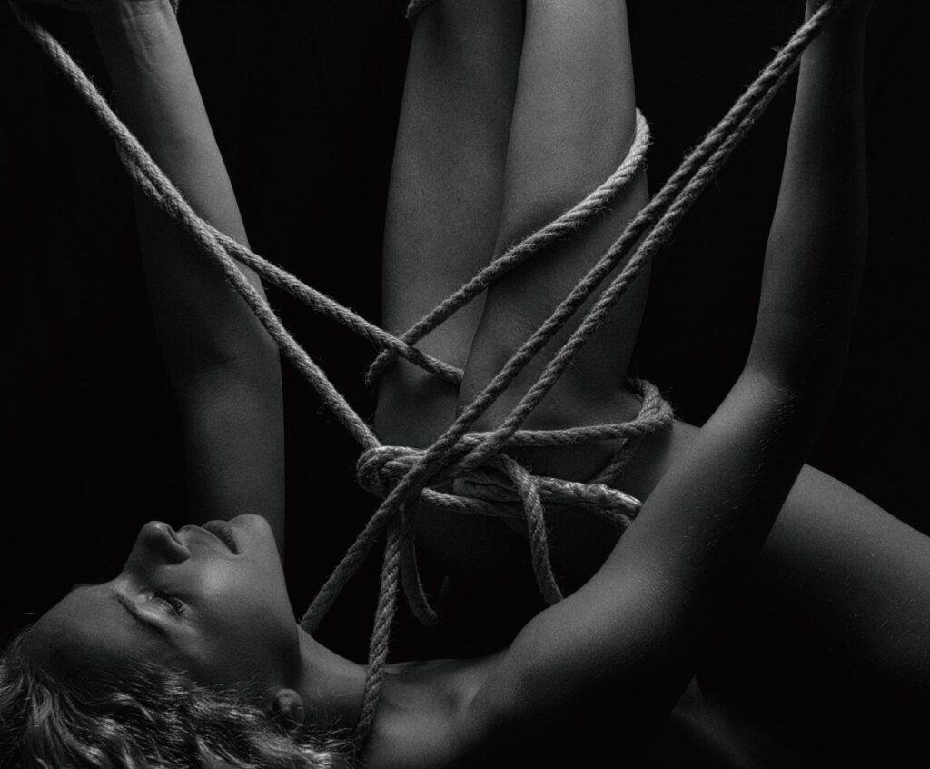 Black and white artistic photo of a woman tied with ropes, evoking conceptual themes.